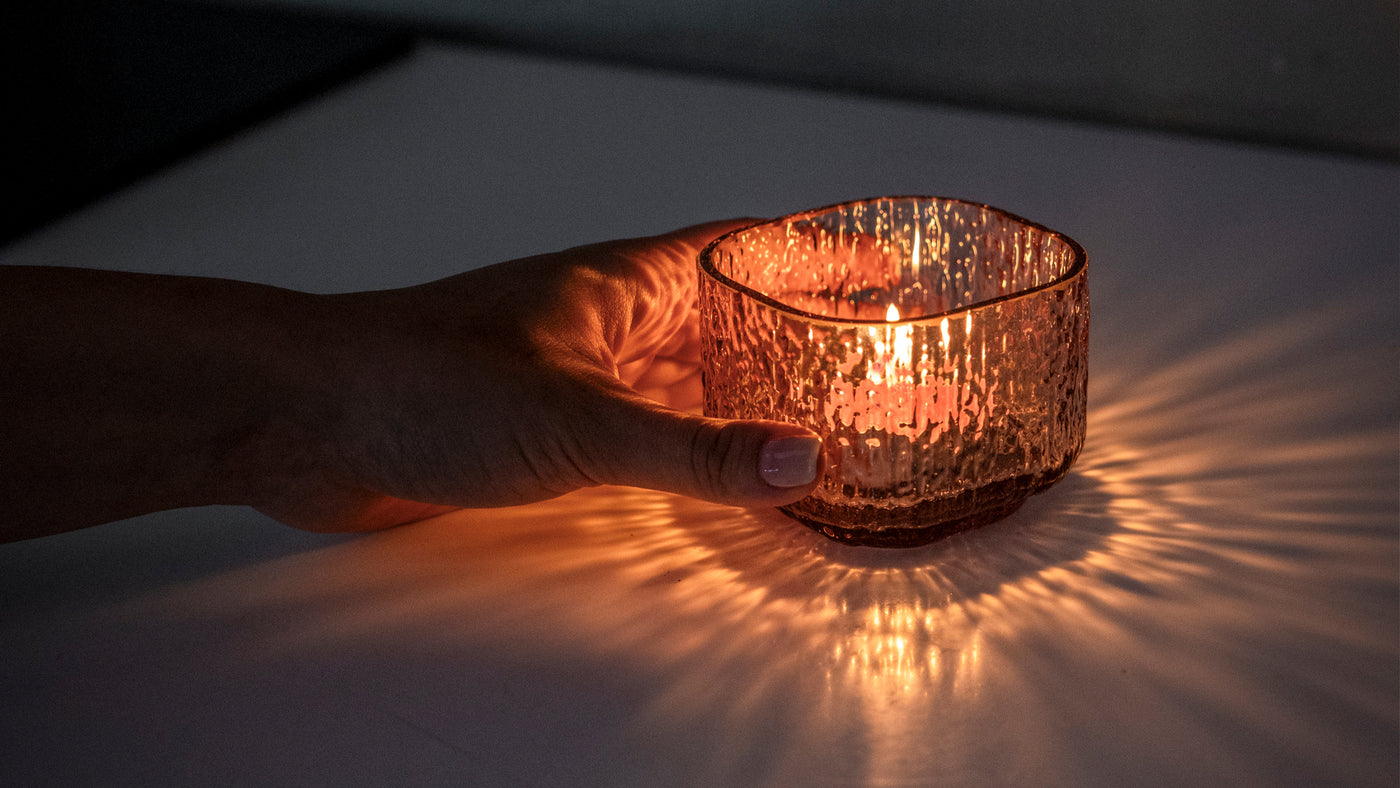 Kuvassa nainen pitelee Kuulea-kynttilälasia pöydällä. Ohjaus kynttilät ja kynttilänjalat -tuotekatgoriaan.