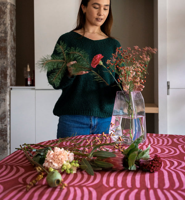 Kuvassa nainen asettelee kukkia vaaleanpunaiseen Lohkare-maljakkoon. Ohjaus joulusesongin tuotteet -collectionille.
