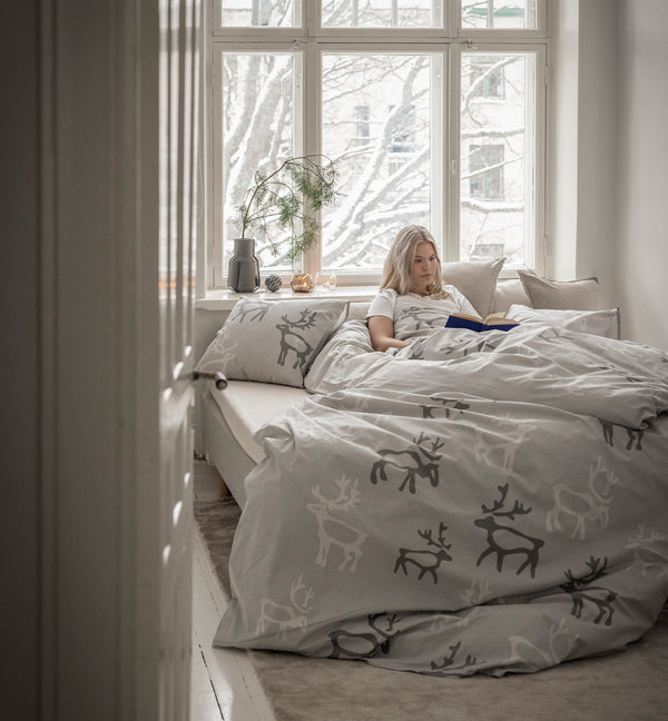 Nainen lukee kirjaa Saaga-vuodevaatteissa. Ohjaus Joulun tekstiilit -tuotekatergoriaan.