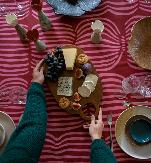 Kuvassa kädet asettamassa juustotarjotinta pöytään, jolla on punainen Vilja-pöytäliina. Ohjaus joulusesongin tuotteet-collectionille.